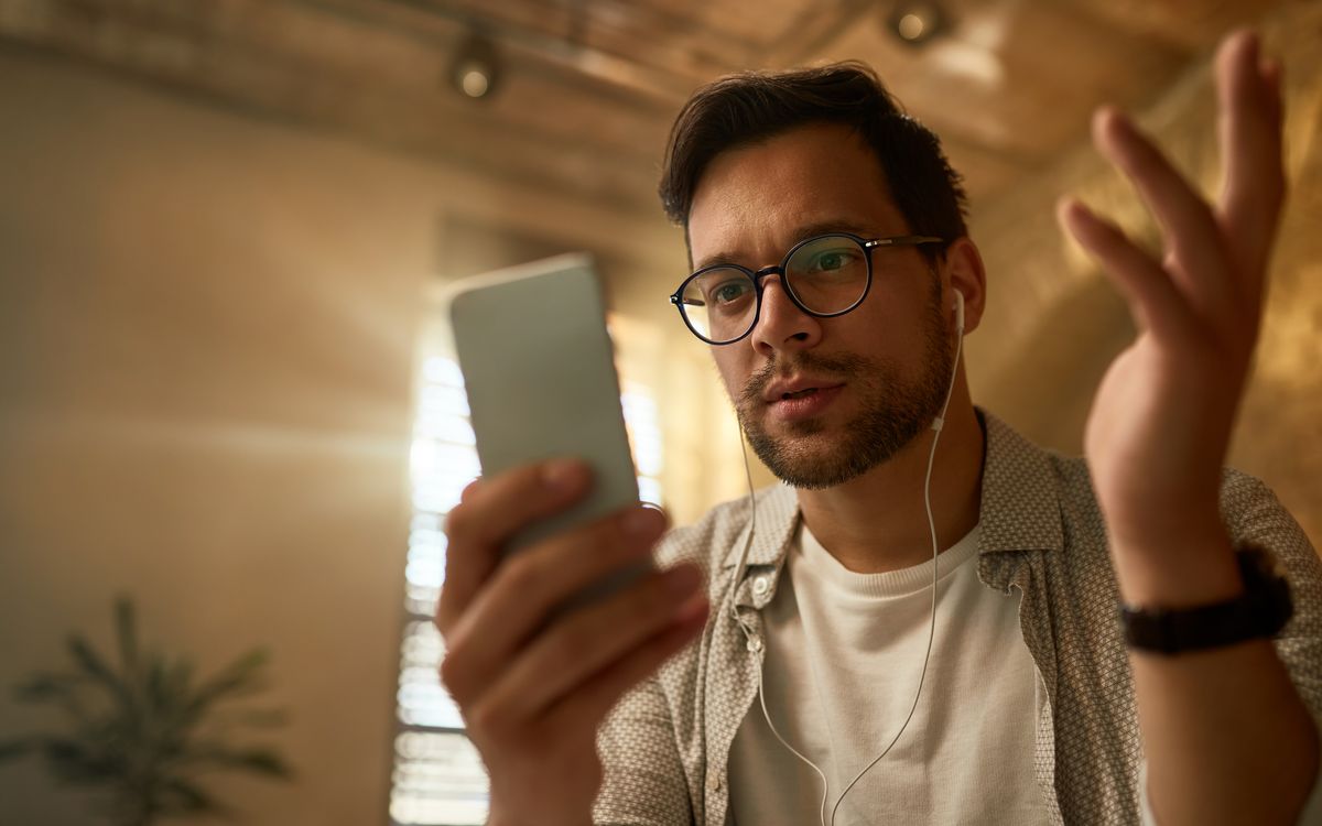 Homem confuso olhando para o celular, com fone de ouvido e gesticulando